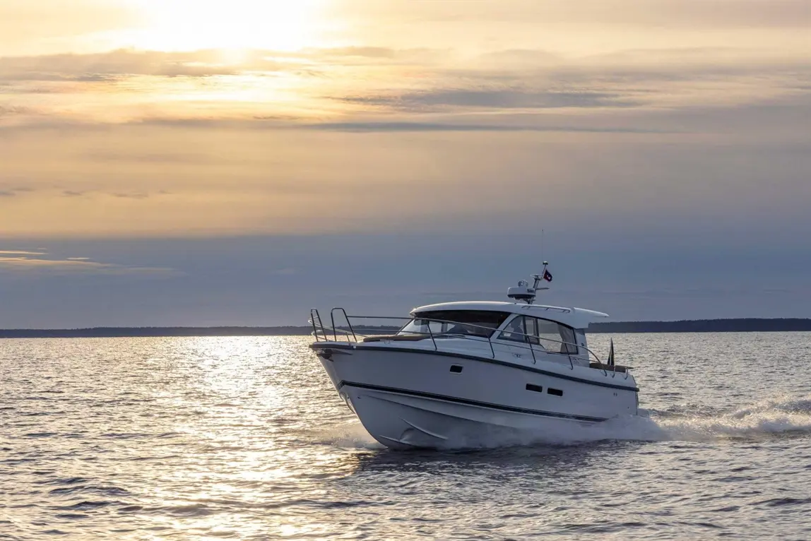 A white motorboat glides across shimmering water during sunset, with soft clouds illuminated by the waning sun.